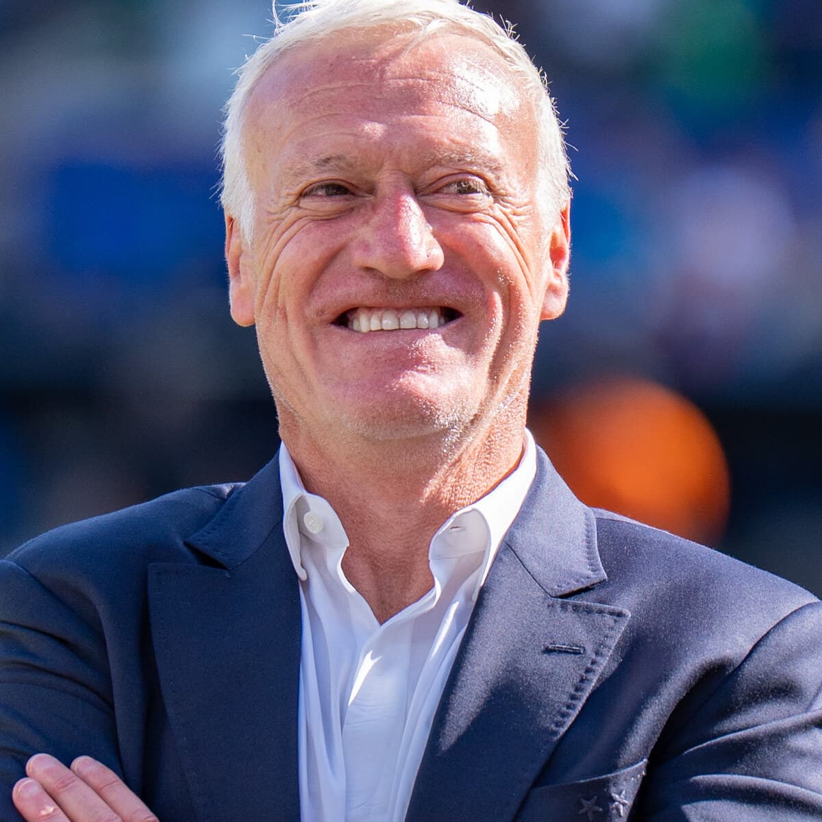 Didier Deschamps souriant en costume aux deux étoiles au bord de la pelouse pendant le Mondial 2026